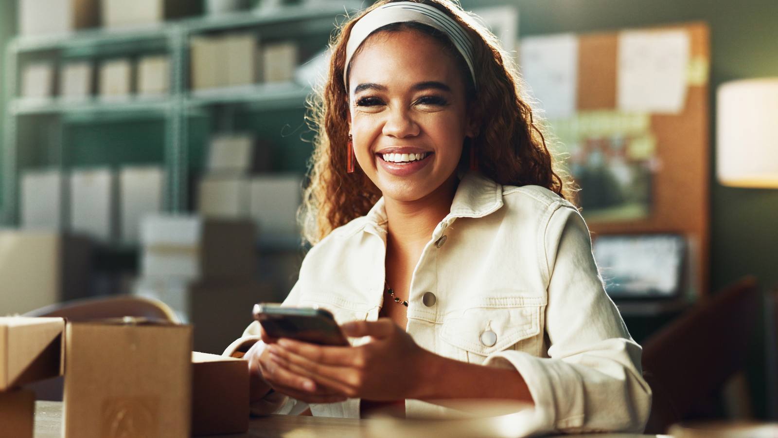 Créatrice souriante qui gère sa boutique TikTok Shop sur son téléphone, entourée de cartons de commandes