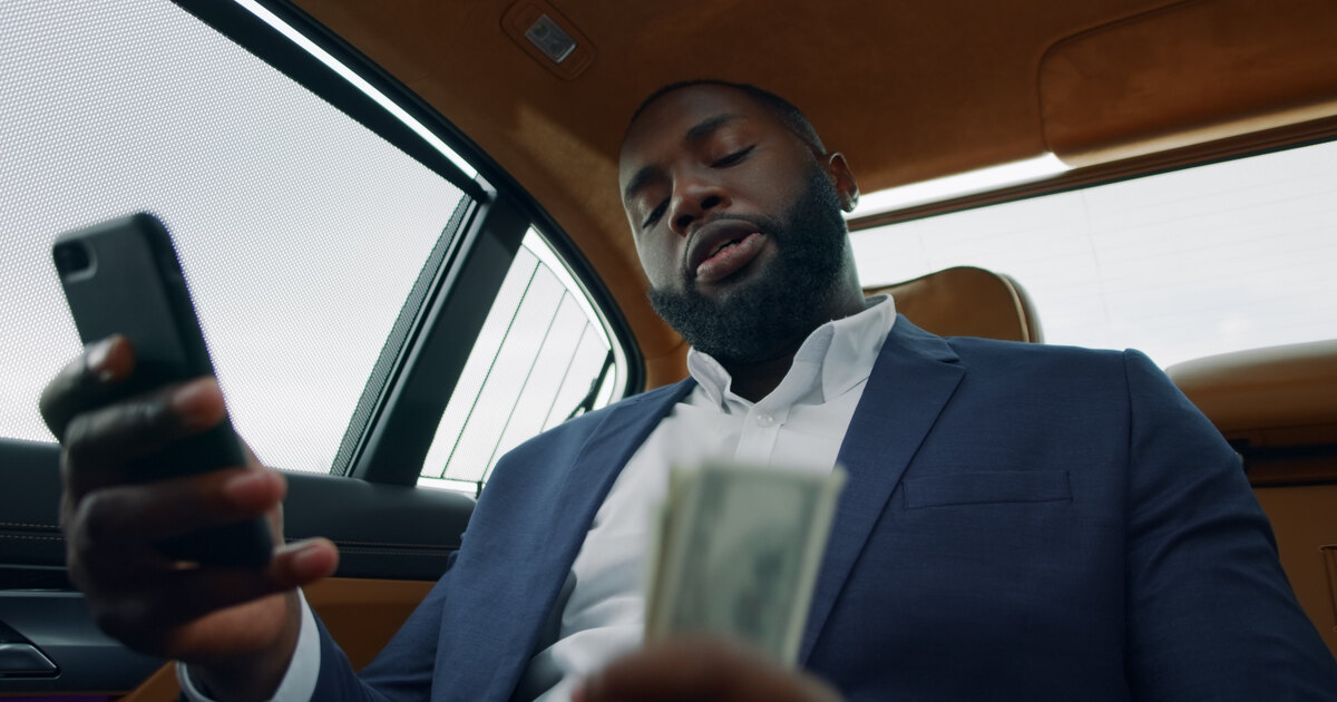 Homme en costume comptant des billets avec son téléphone à la main, lumière cinématique