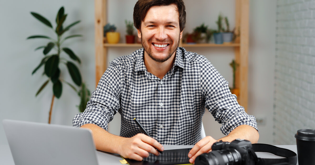 Créateur souriant travaillant sur son ordinateur portable avec sa caméra, montage de contenu