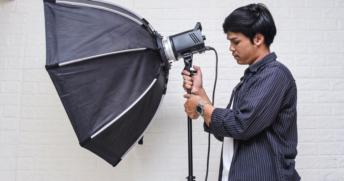 Créateur qui règle une softbox octogonale devant un mur clair, éclairage de studio maison