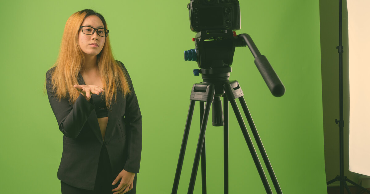 Créatrice devant un fond vert avec sa caméra sur trépied, en studio maison