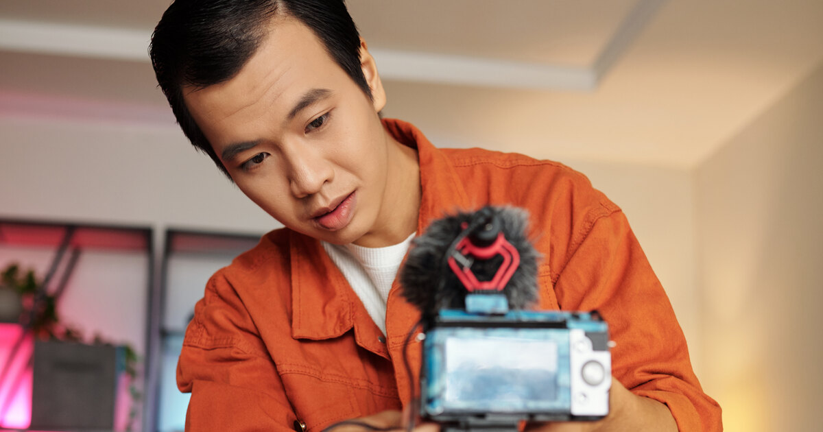 Jeune créateur asiatique ajustant sa caméra équipée d un micro dans un intérieur chaleureux
