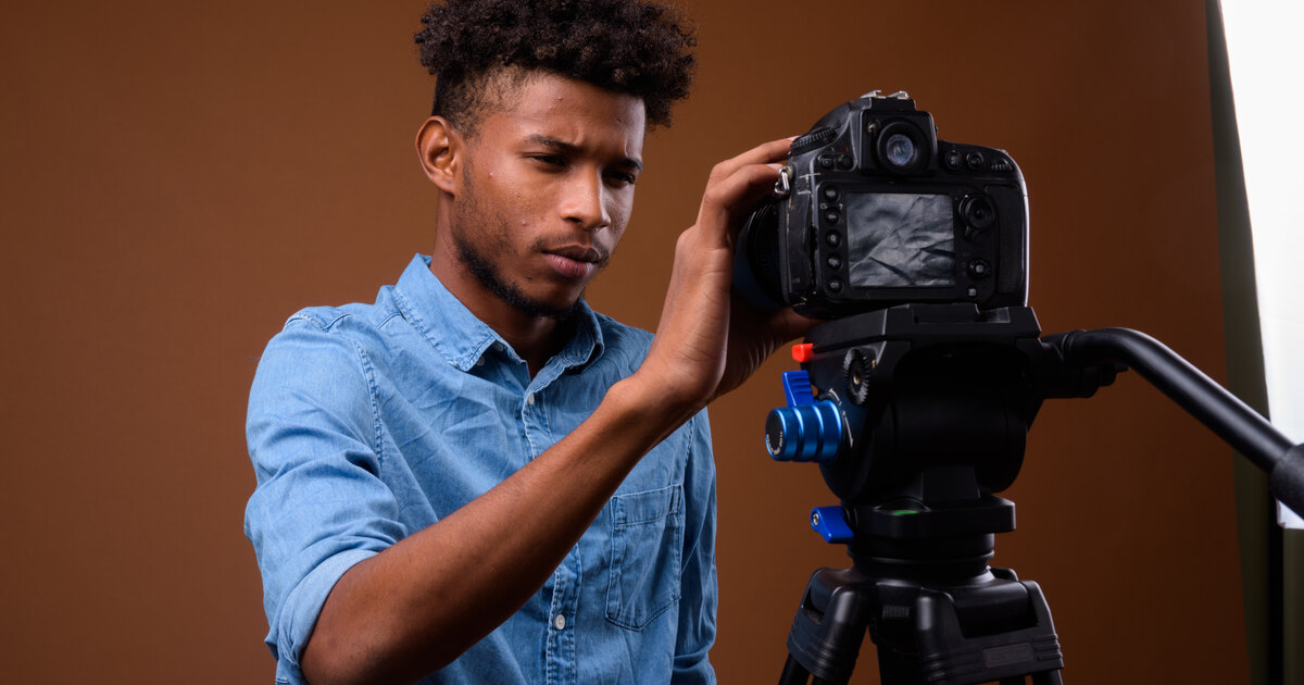 Jeune créateur africain réglant son appareil reflex sur un trépied en studio