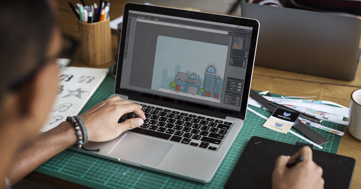 Créateur qui conçoit un graphisme sur son ordinateur portable avec une tablette à stylet