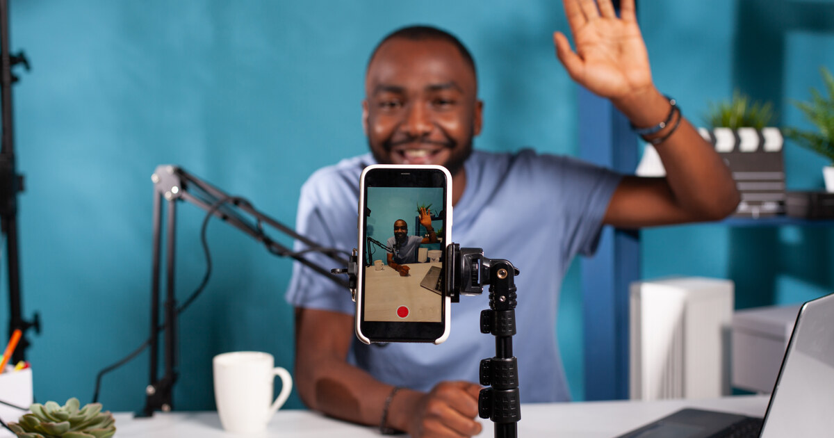 Créateur en direct qui salue ses abonnés, filmé par son téléphone posé sur un trépied