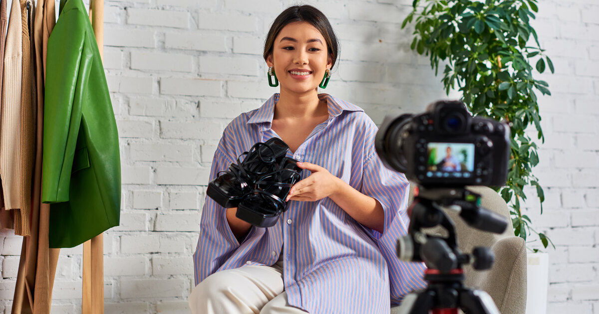 Jeune créatrice asiatique souriante filmant une vidéo avec un appareil photo sur trépied dans un intérieur clair