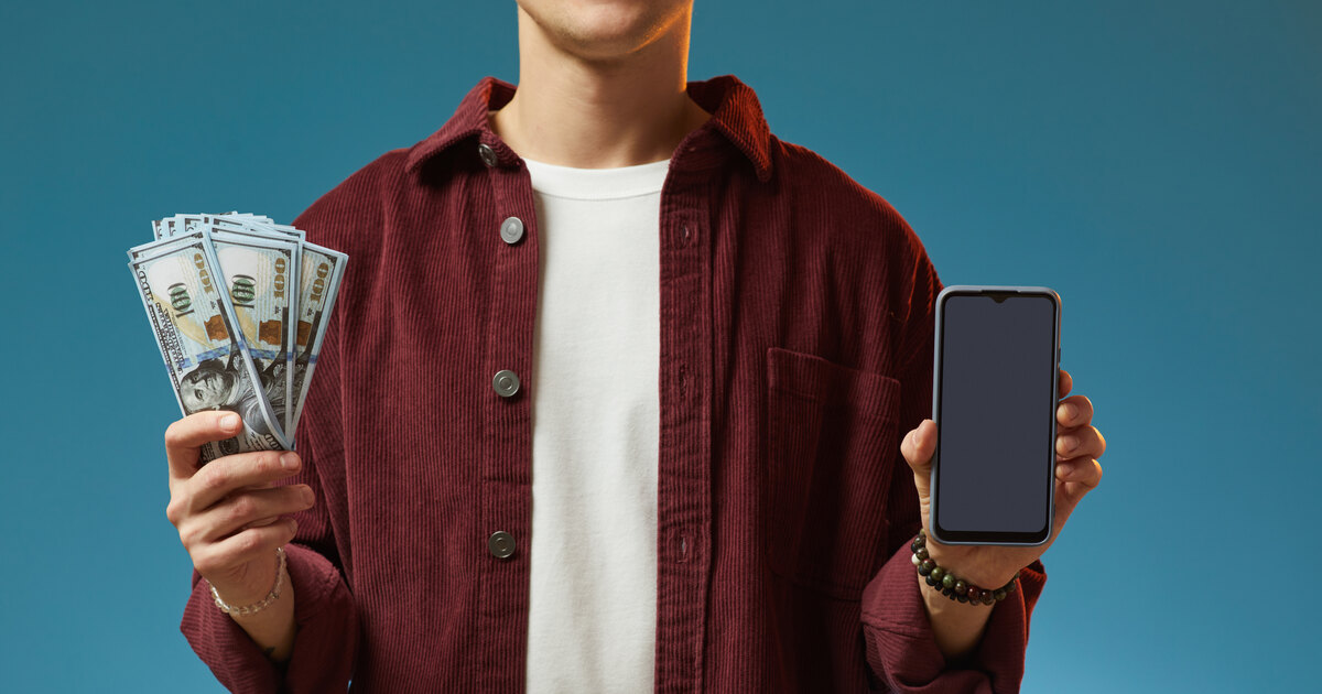 Jeune homme souriant tenant des billets et un smartphone, retrait de ses gains