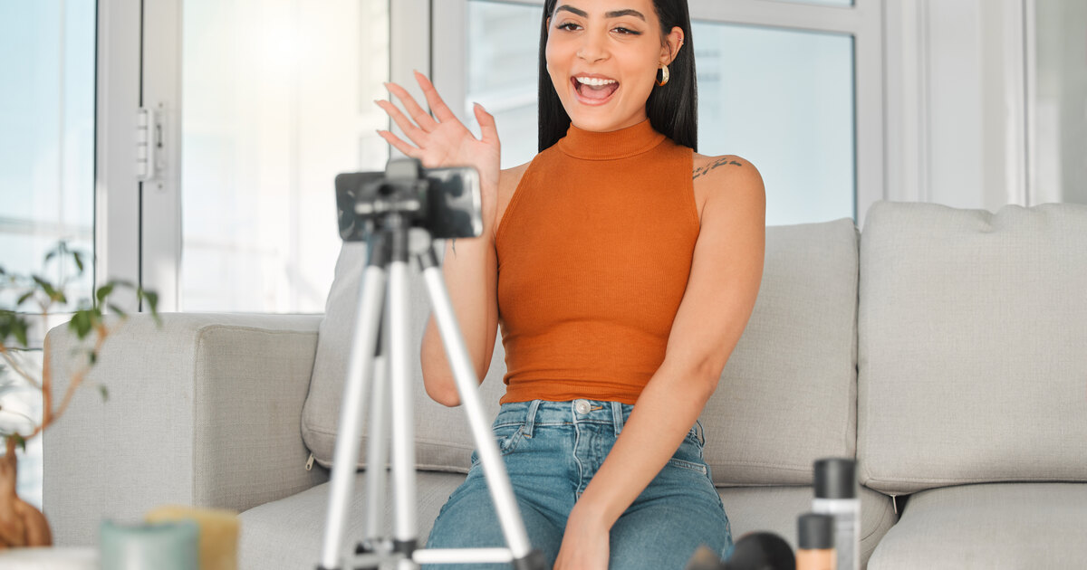 Jeune créatrice latina souriante en direct devant un téléphone sur trépied dans un salon lumineux