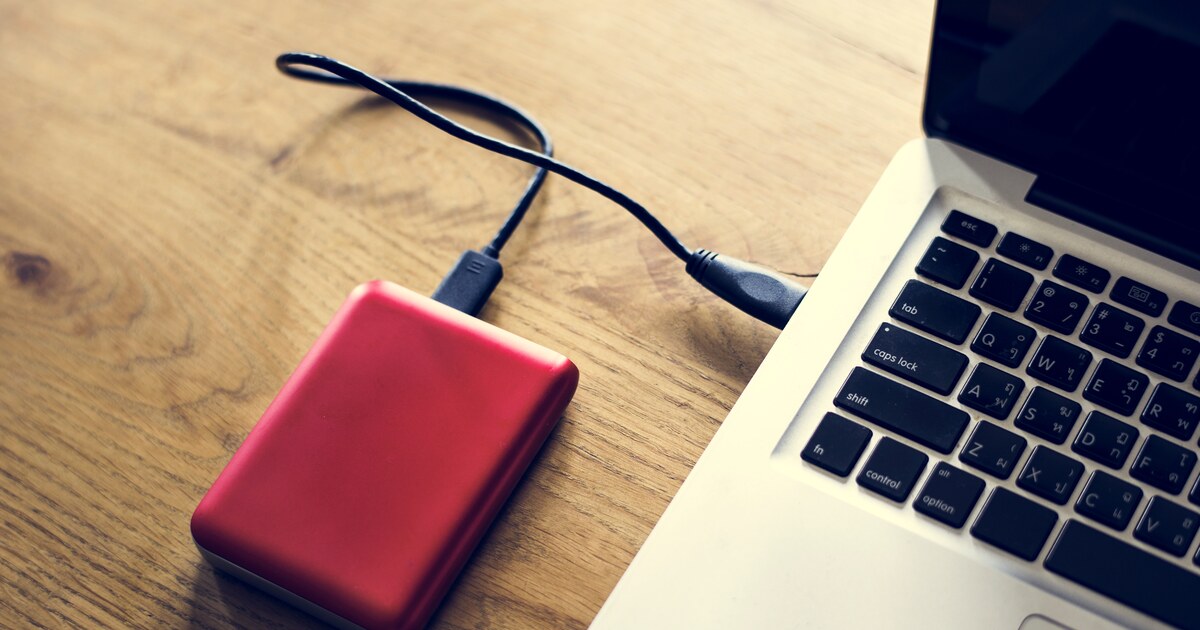 Disque dur externe relié à un ordinateur portable sur un bureau en bois, pour sauvegarder ses fichiers
