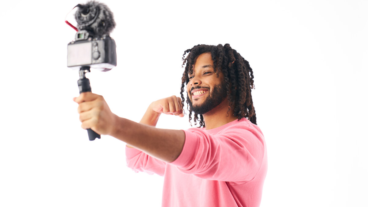 Créateur souriant filmant une vidéo et un live avec une caméra sur poignée, fond clair