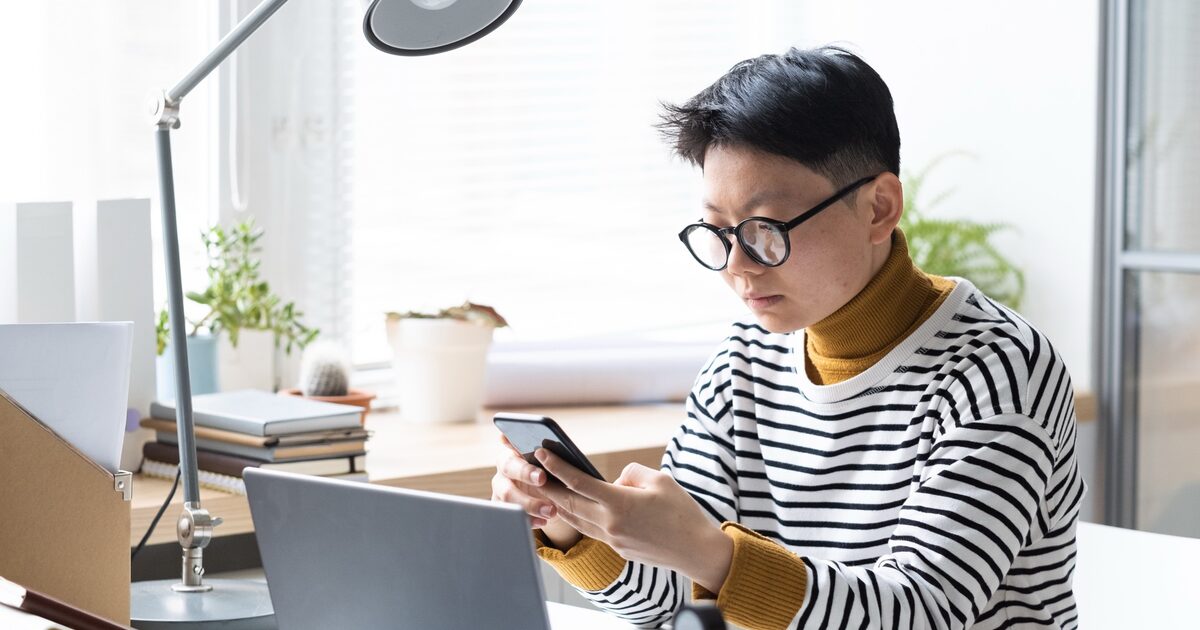 Personne qui vérifie son site depuis son téléphone, à côté de son ordinateur