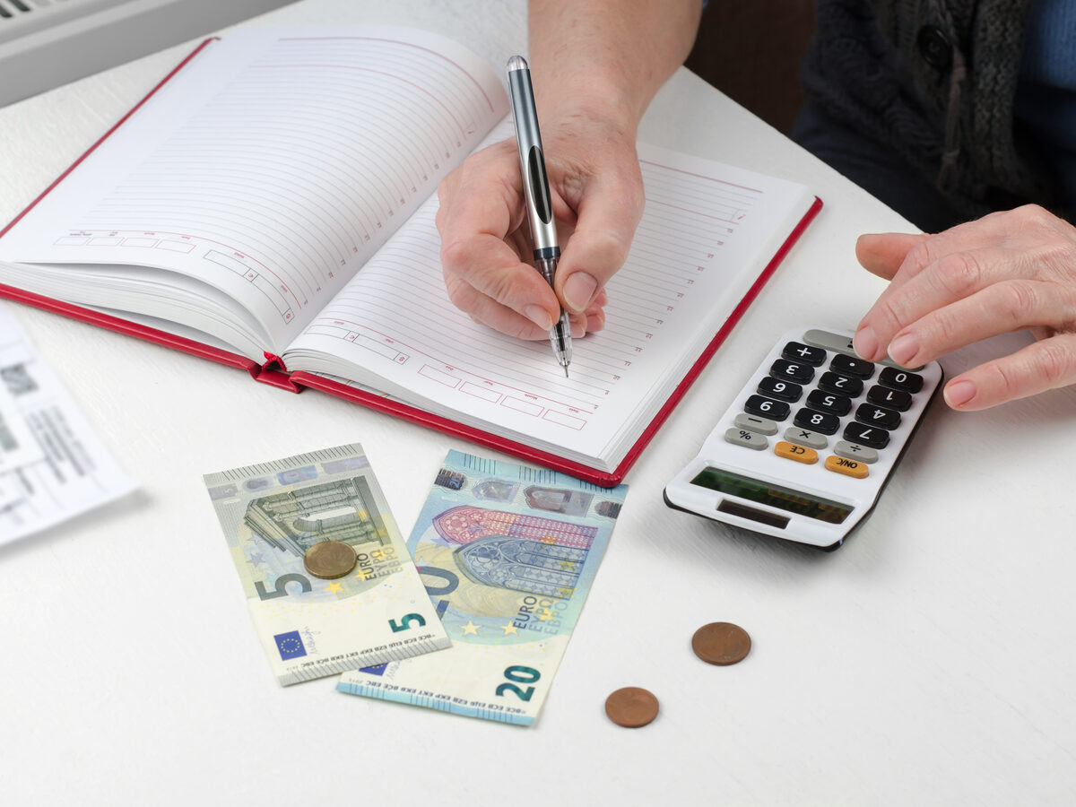 Mains qui font leurs comptes avec un carnet, une calculatrice et des euros