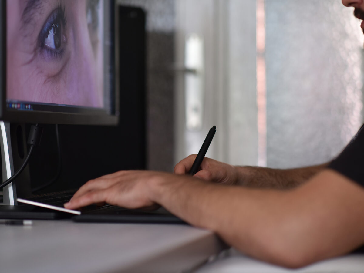 Main sur une tablette graphique devant un portrait à retoucher