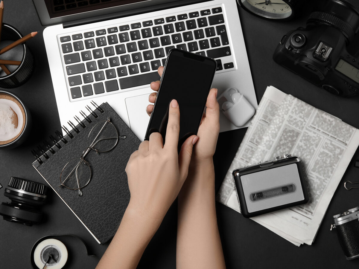 Mains sur un téléphone, au milieu d'un bureau avec appareil photo et ordinateur