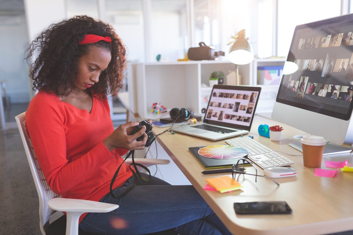 Femme à son bureau qui prépare ses photos sur son ordinateur et son portable