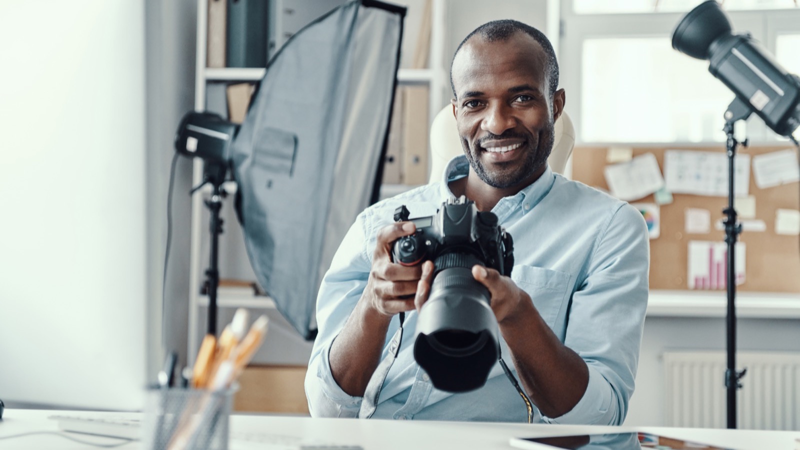 Créateur souriant tenant son appareil photo, softbox et flash de studio derrière lui