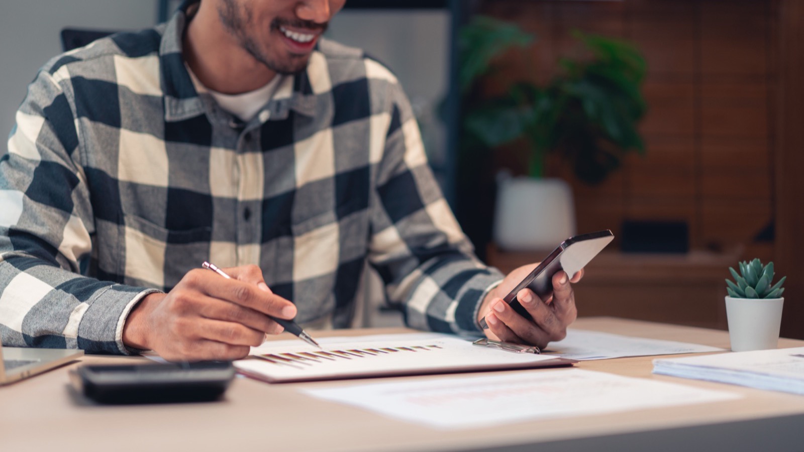 Créateur qui fait ses comptes : calculatrice, carnet et téléphone posés sur son bureau