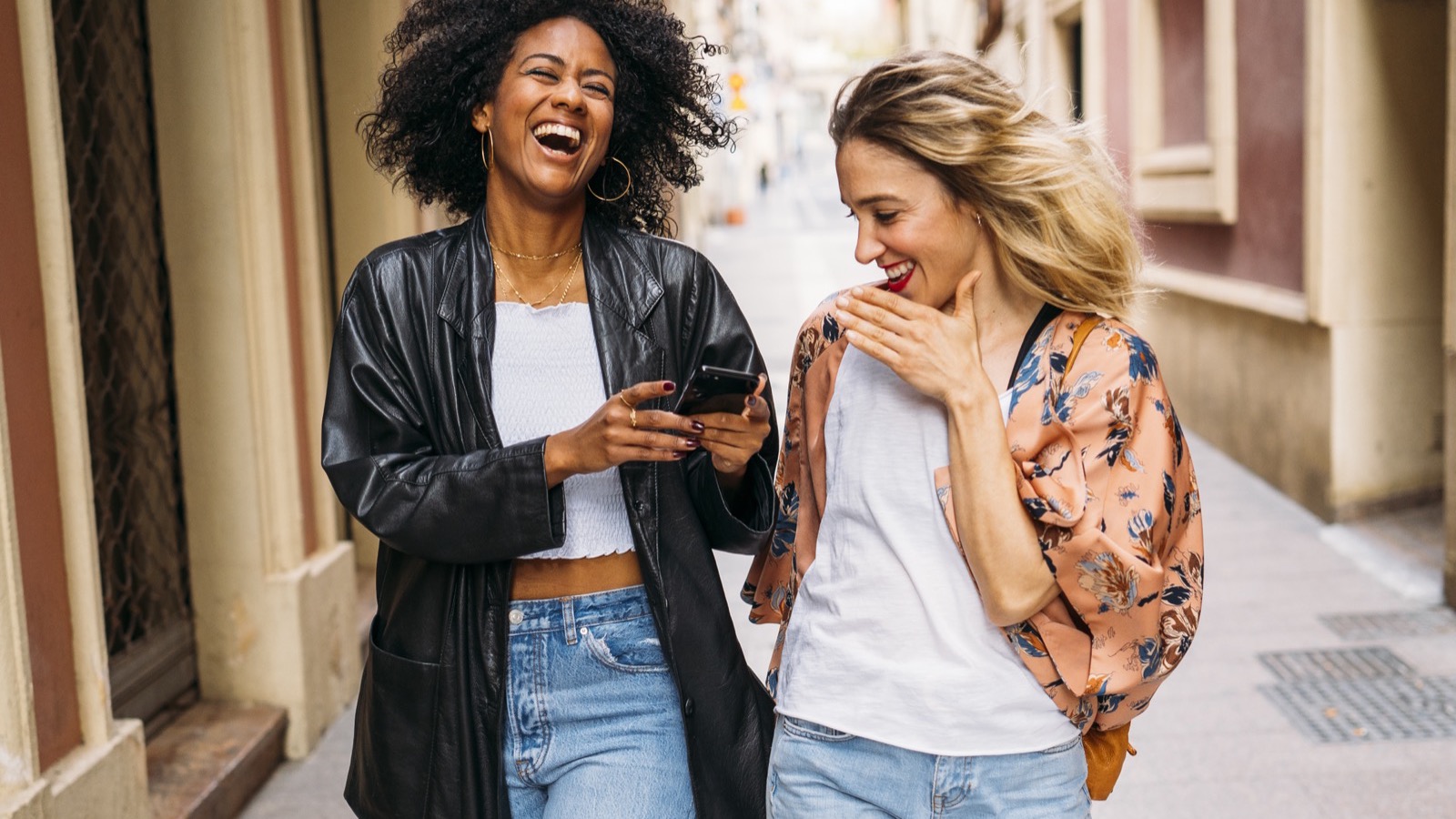 Deux amies qui rient en se partageant un lien sur un téléphone, dans la rue