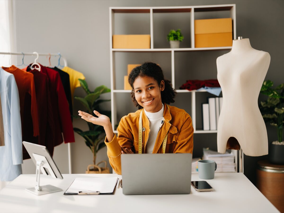 Une couturière travaille à son bureau, son ordinateur portable ouvert dans son atelier